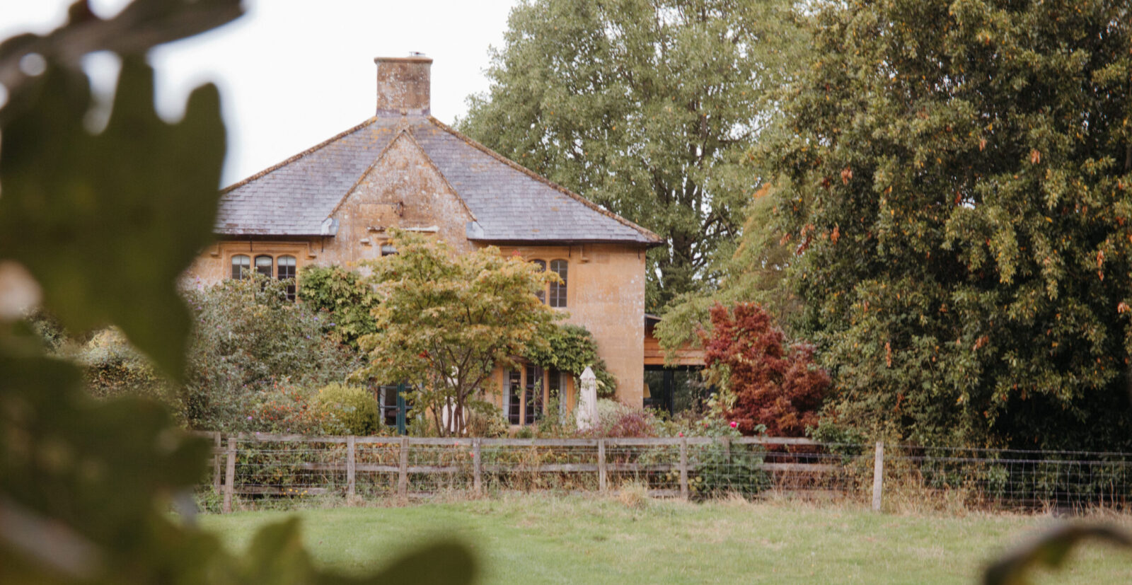 A beautiful country house surrounded by trees and a. fence by a field