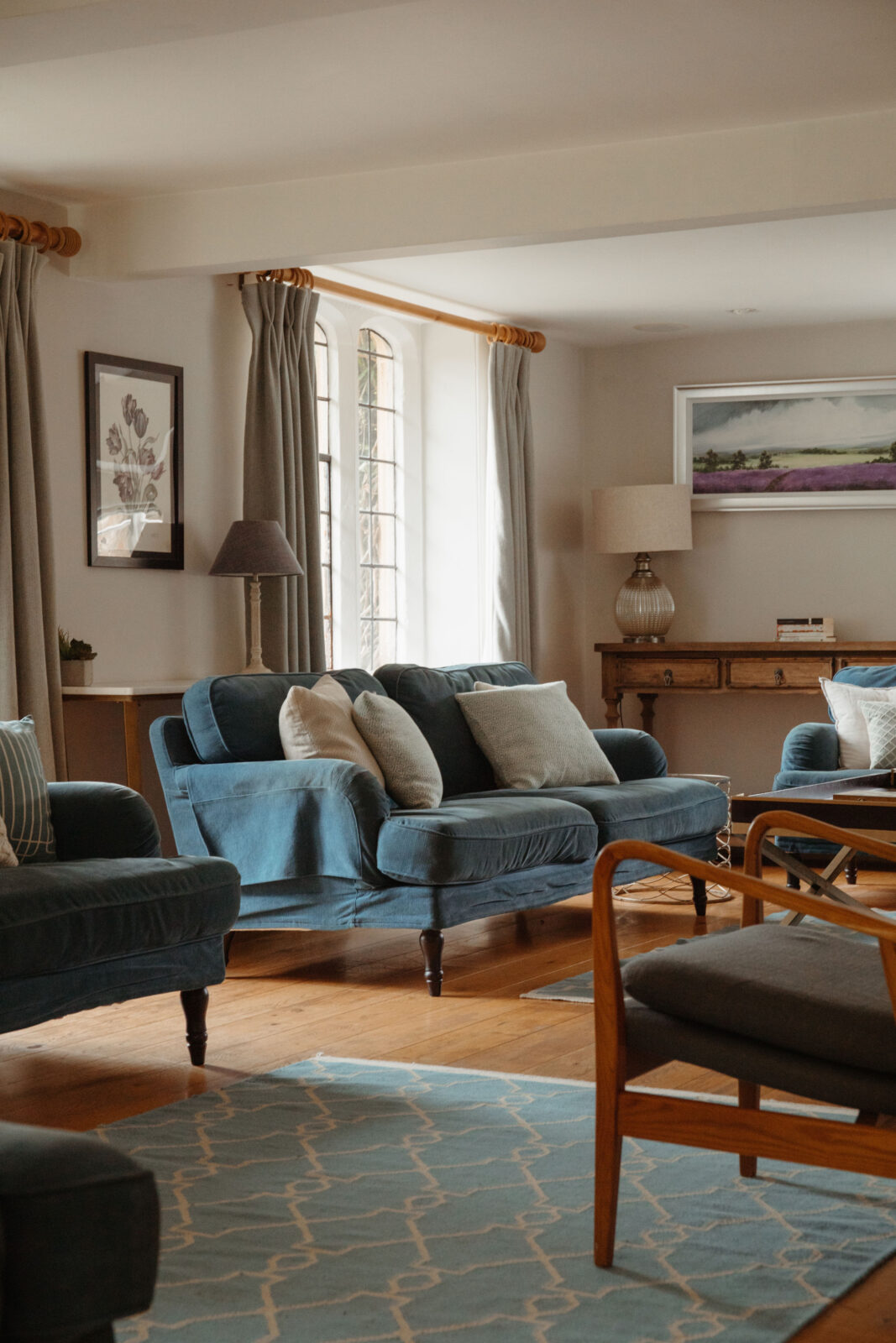 Country house style living room with a blue sofa, wooden floors, stylish lamps, and large windows