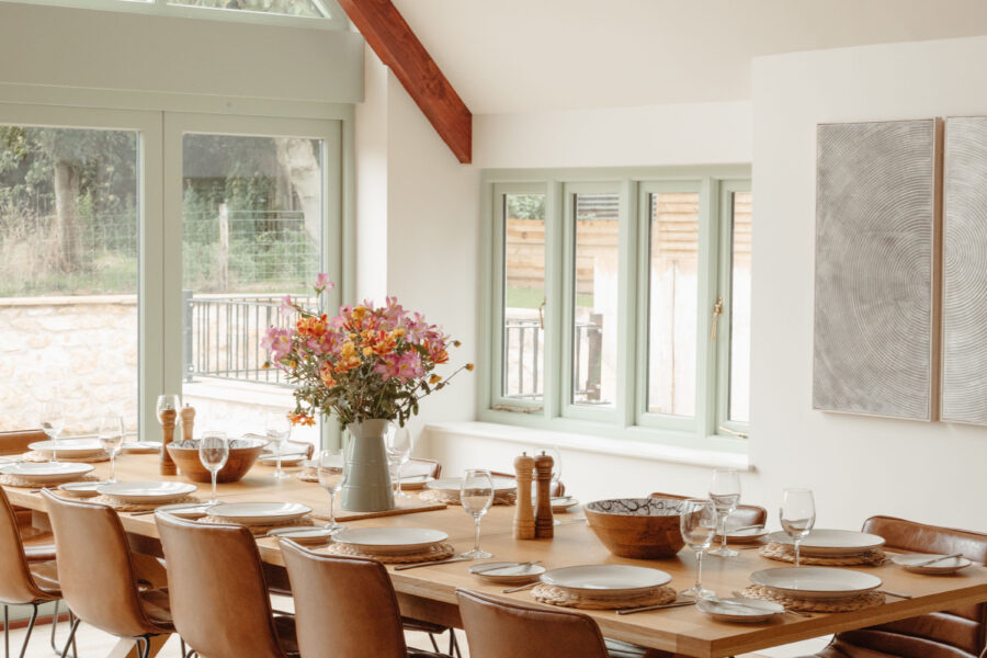 Long modern dining table laid with white plates, wine glasses and wild flowers