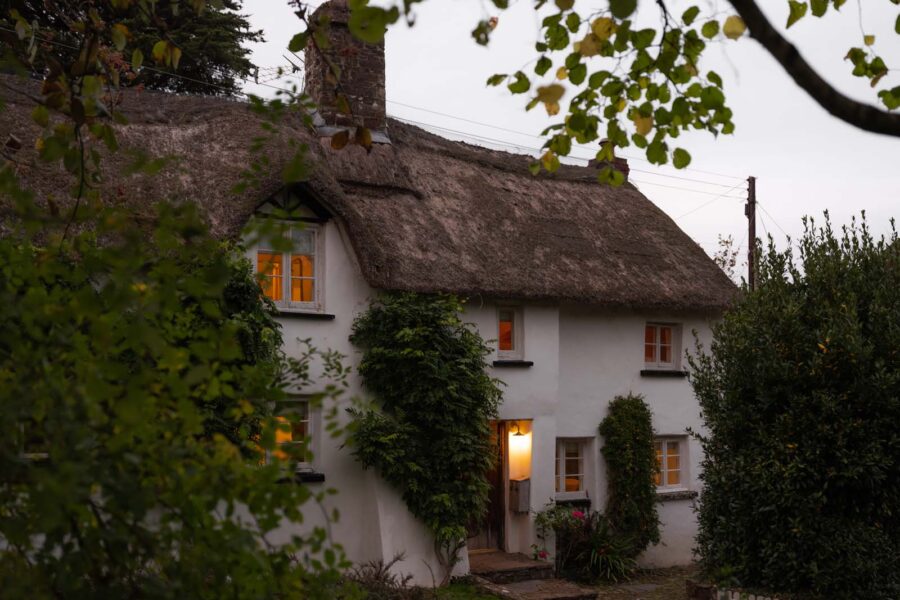 A cosy thatched cottage at dusk with lights on inside