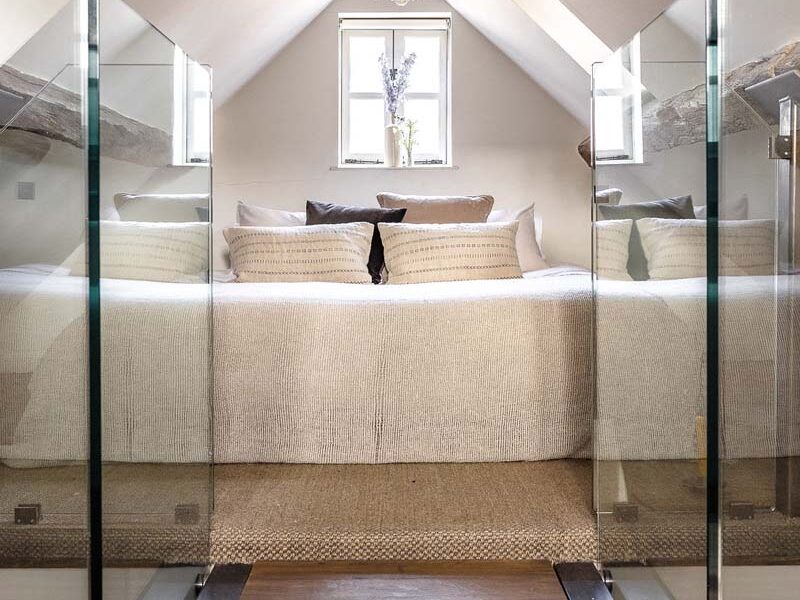A bridge with glass sides leading towards a bedroom in the eaves