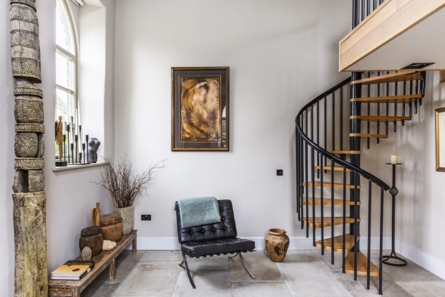 A room with a winding wooden staircase, modern furniture, bohemian decor and white walls