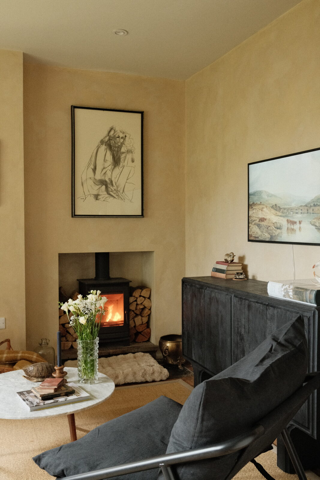 Living room featuring artworks in a traditional yet modern style with a cosy wood burner.